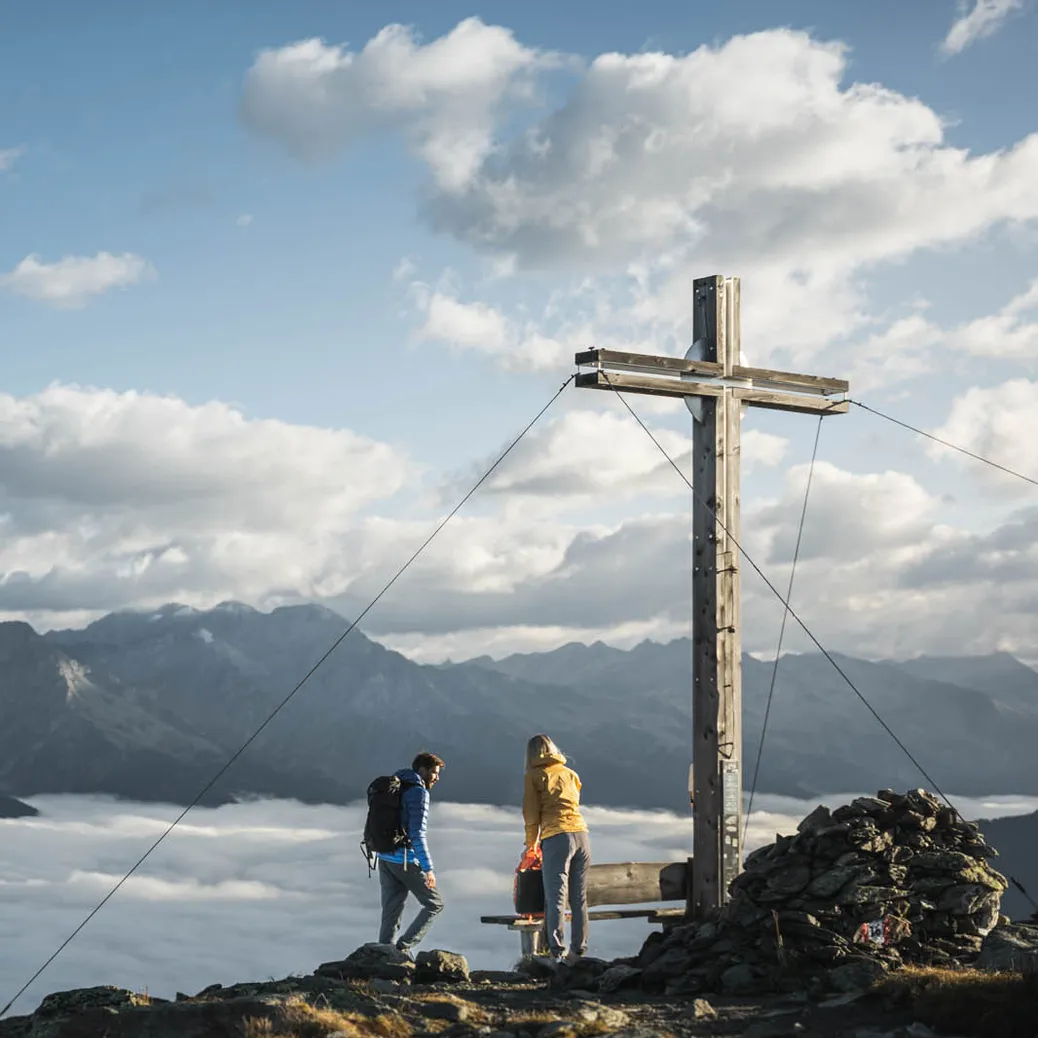 Hiking couple at summit cross above sea of clouds with panoramic view of the South Tyrolean Alps