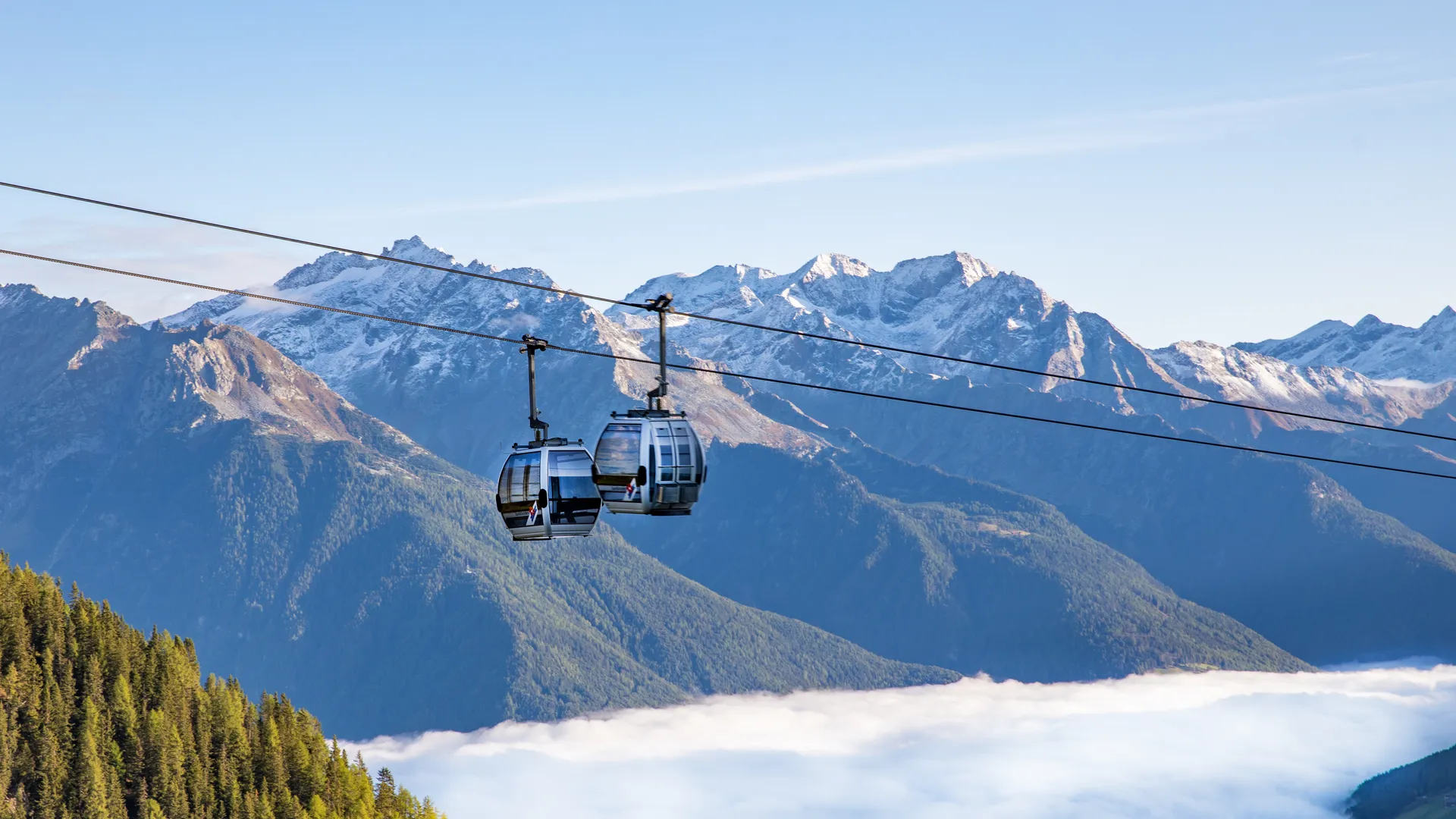 Seilbahnkabinen über dem Nebelmeer im Ahrntal mit schneebedeckten Tauern-Gipfeln im Herbst