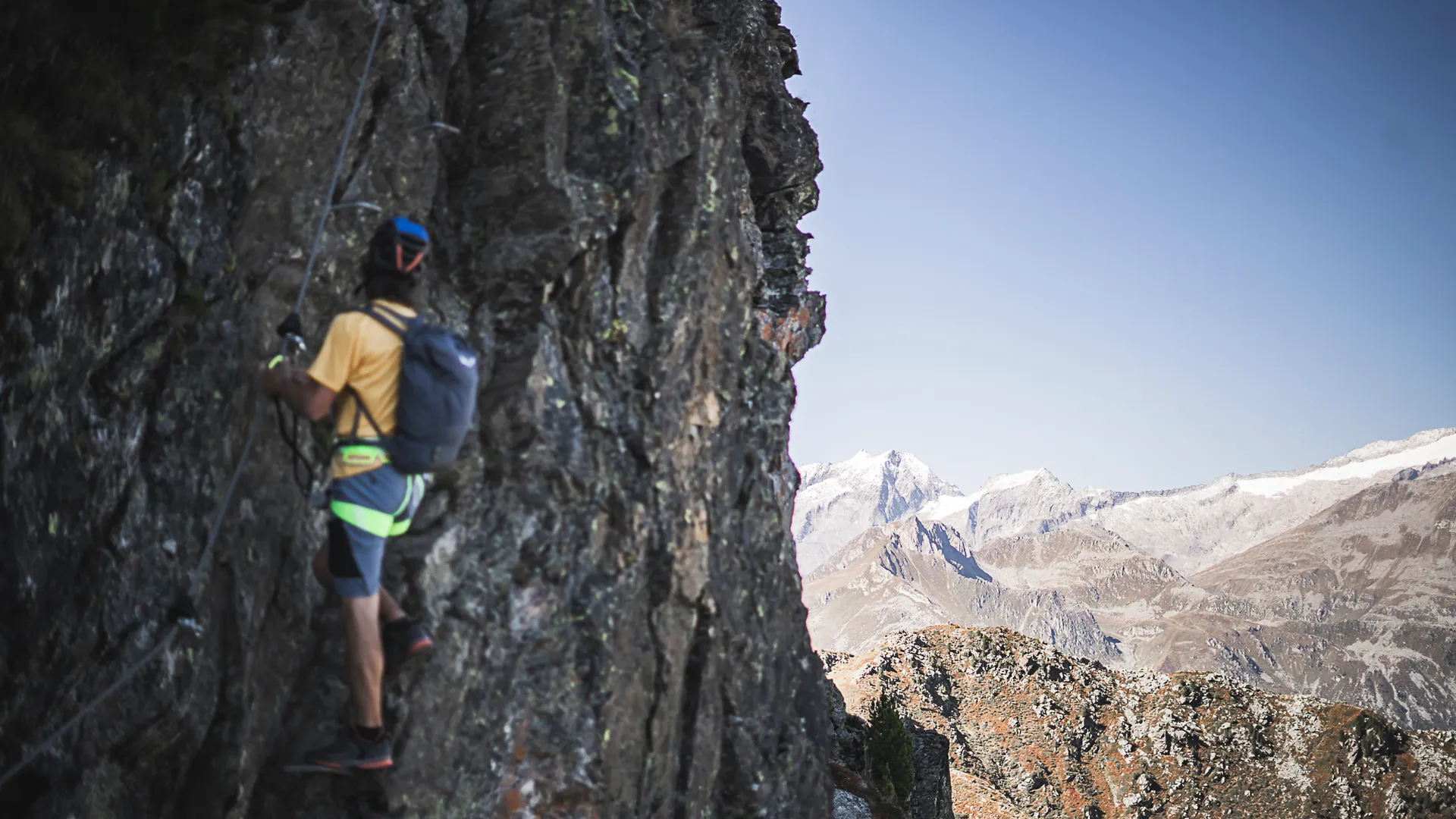 Via ferrata climber with helmet on steep rock face, snow-covered Zillertal Alps in the background
