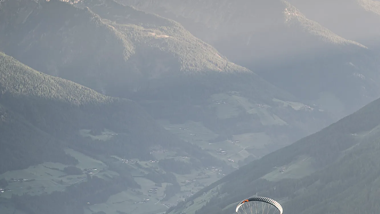 Due parapendii con vele colorate nel sole serale sopra la verde Valle Aurina, Alto Adige