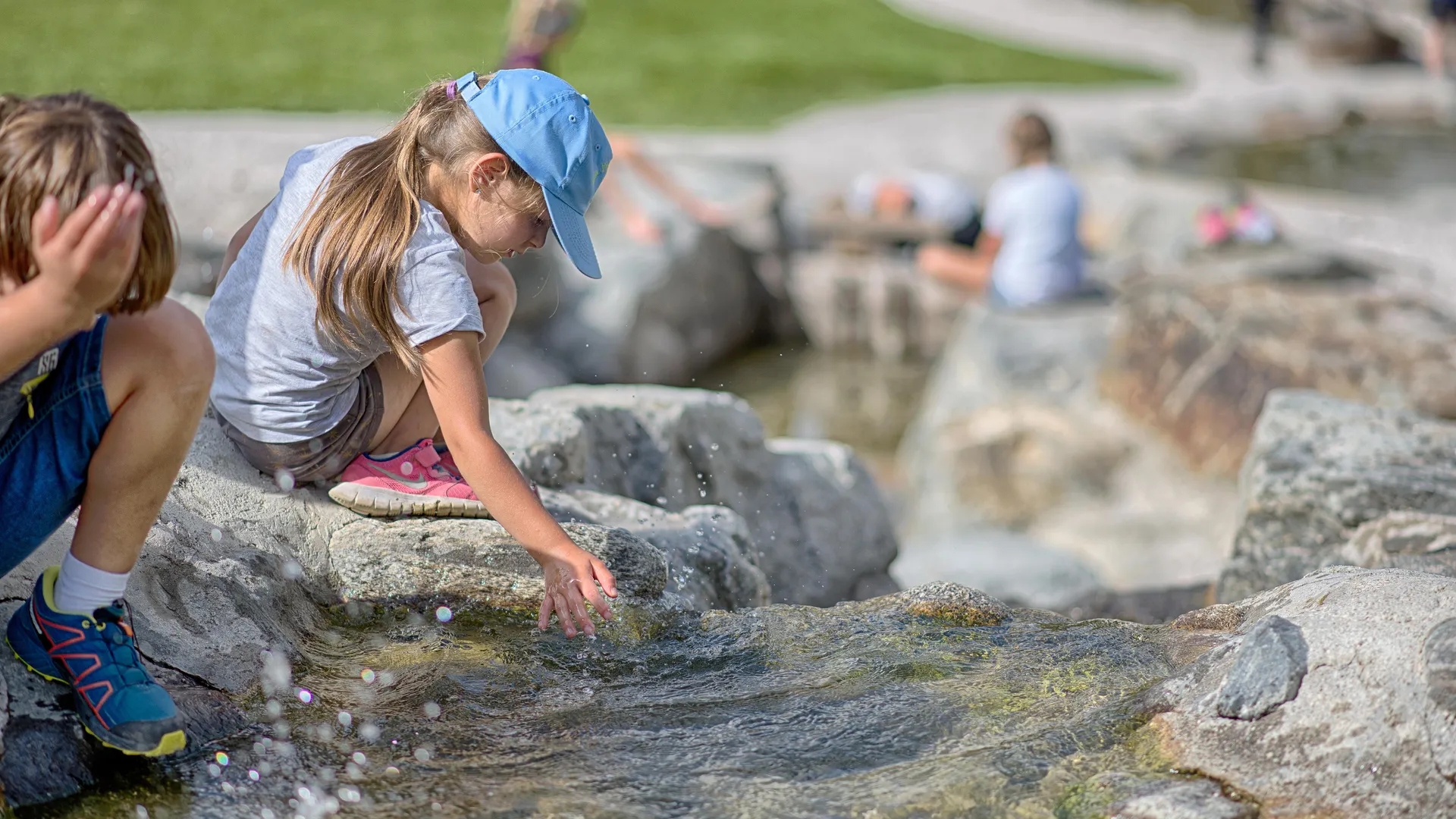 Kinder planschen am Wasserspielplatz im Familienpark Klausberg, Mädchen erkundet klares Bachwasser