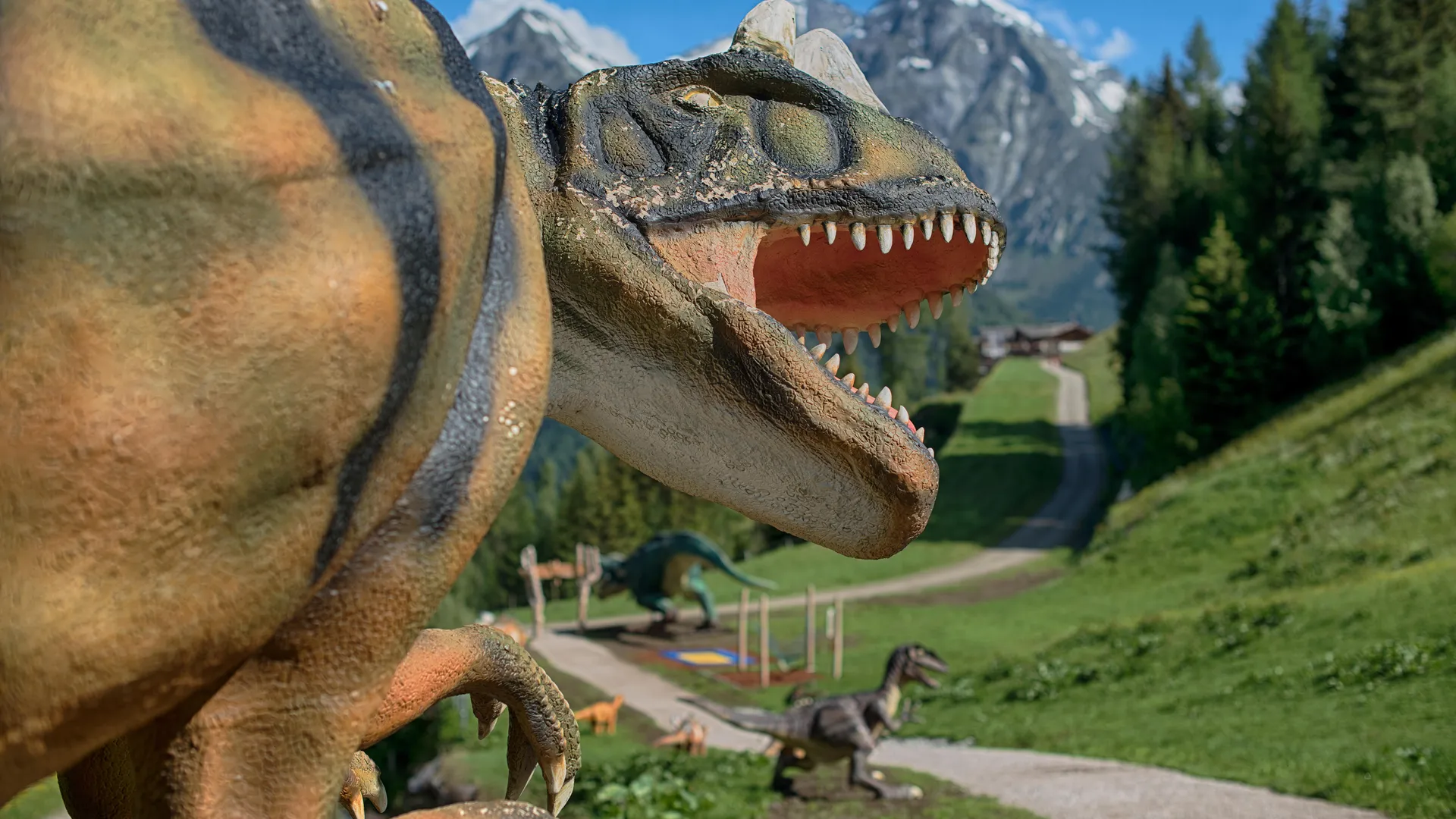 Lebensgroße Allosaurus-Figur mit schneebedeckten Gipfeln der Zillertaler Alpen im Hintergrund am Klausberg