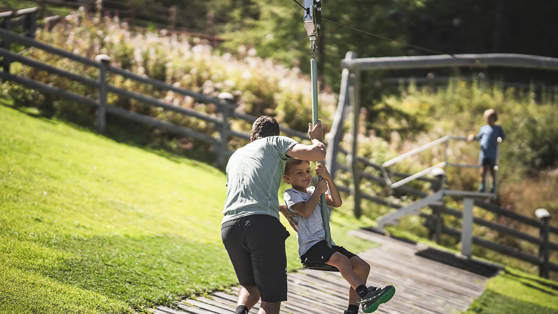Kind auf Seilrutsche am Bergspielplatz Klausberg, Vater hilft beim Anstoßen