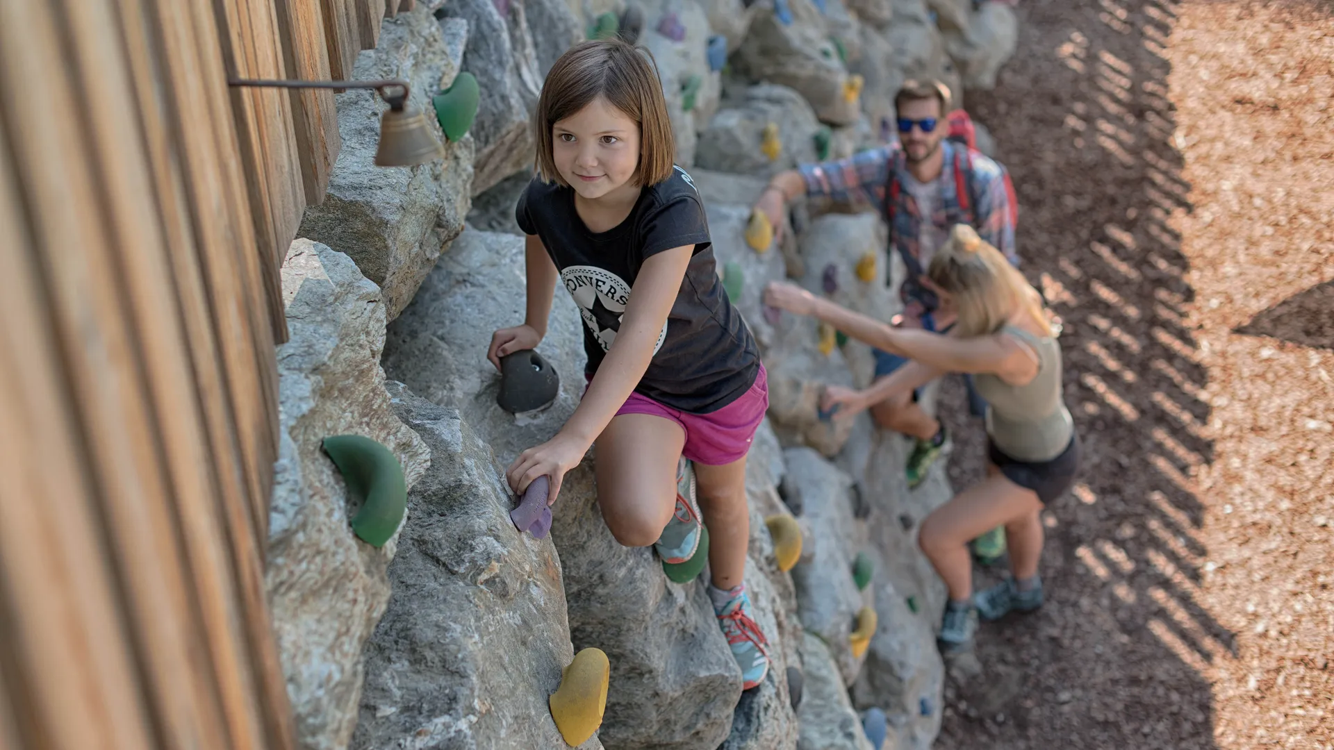 Mädchen klettert konzentriert an großer Outdoor-Kletterwand mit bunten Griffen im Sommer im Ahrntal
