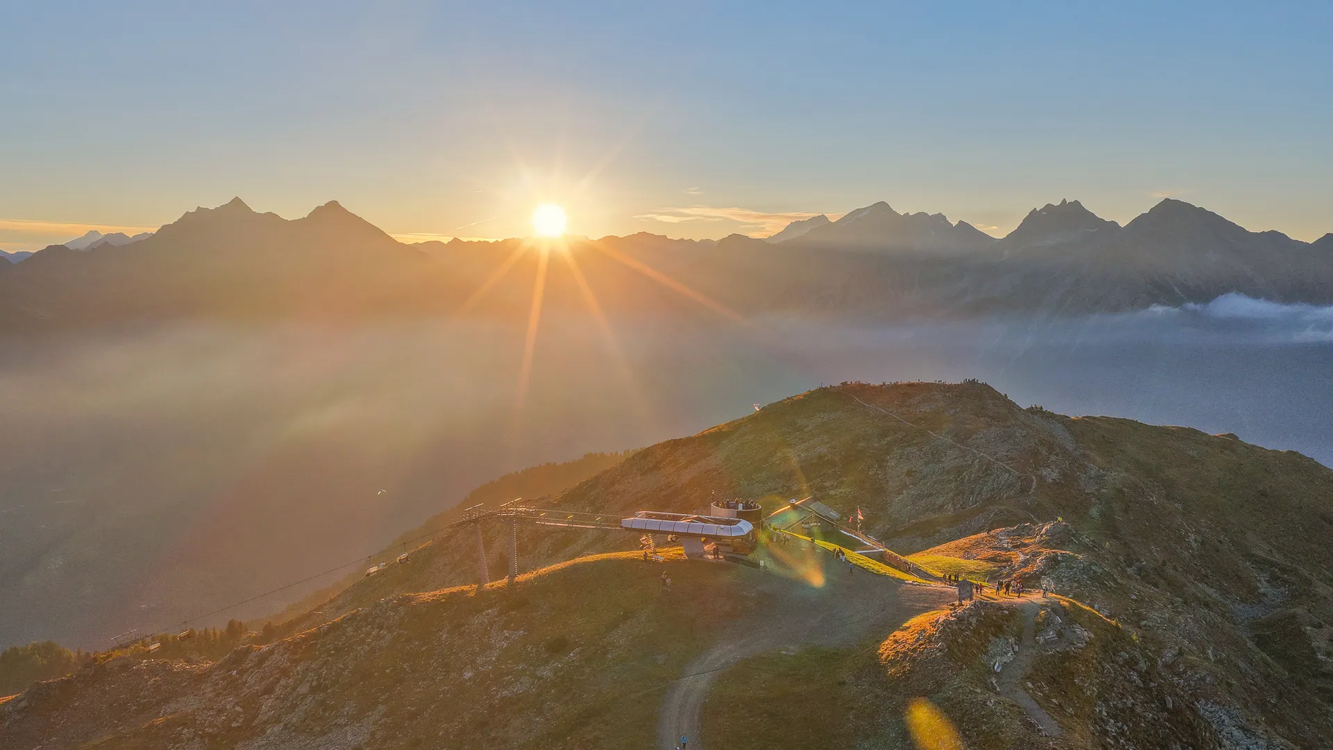Sonnenaufgang an der K1-Bergstation Klausberg mit Nebelmeer im Tal und Paraglider