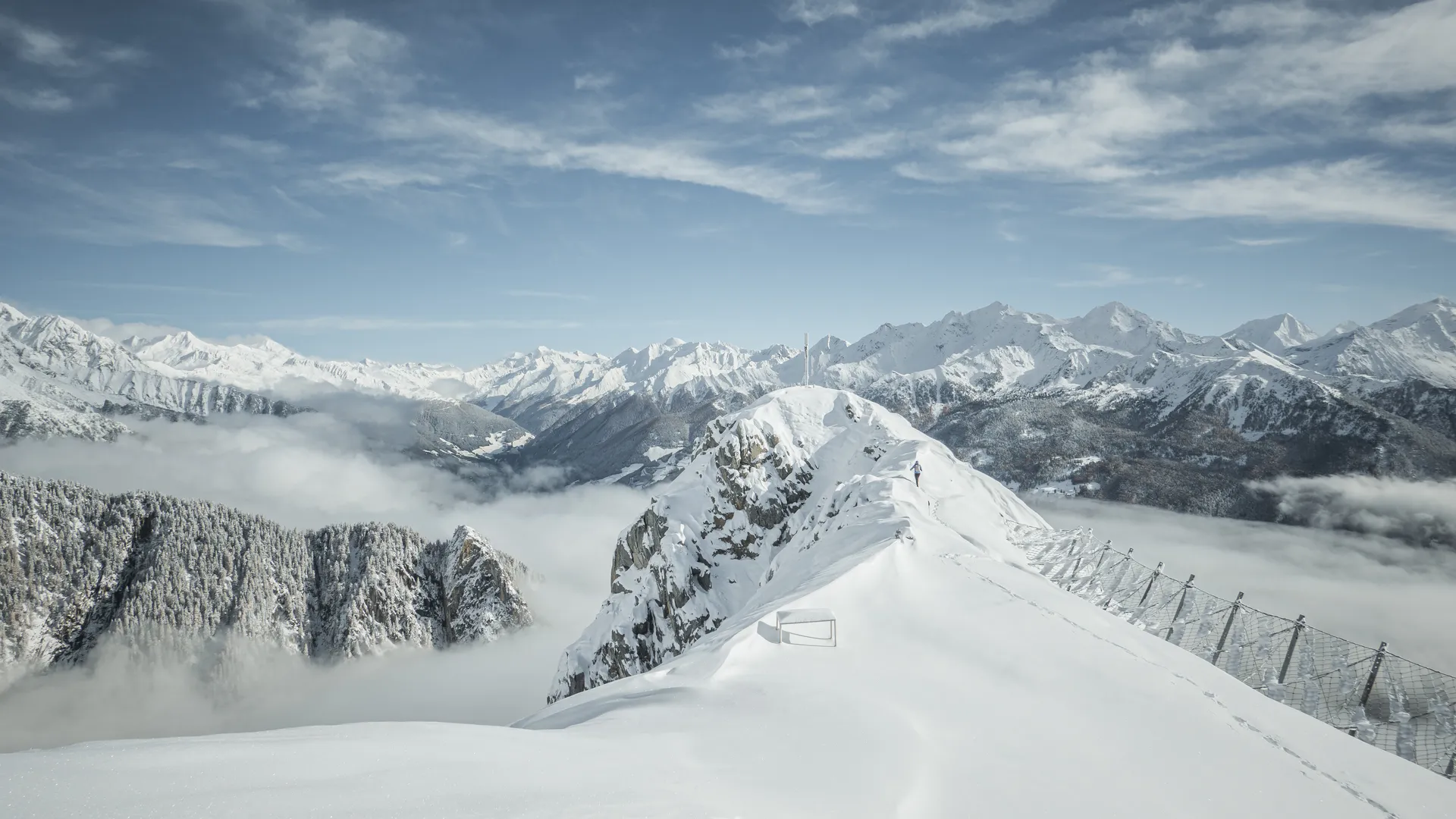 Snow-covered summit ridge with avalanche barriers above fog sea in Ahrntal, Zillertal Alps
