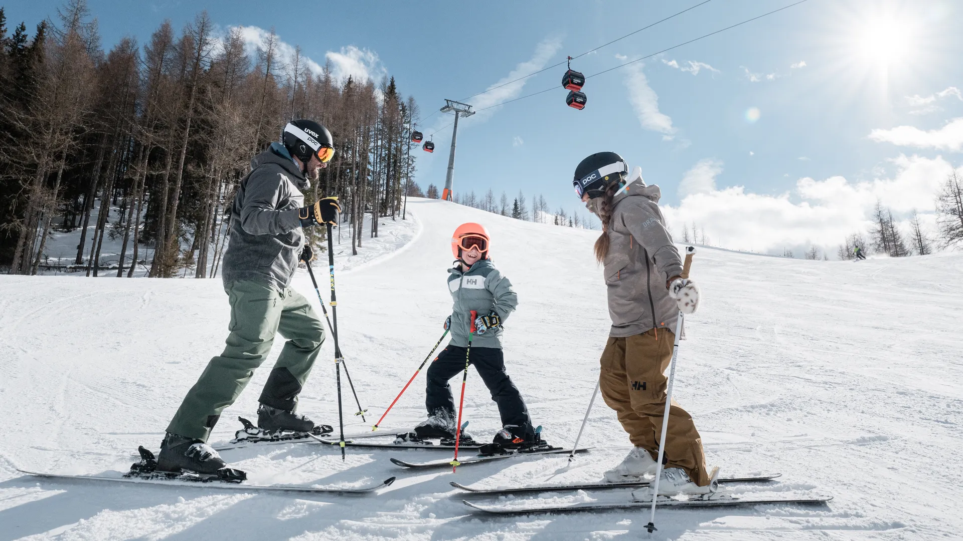 Familie beim Skifahren auf sonniger Piste am Klausberg mit roten Gondeln im Hintergrund