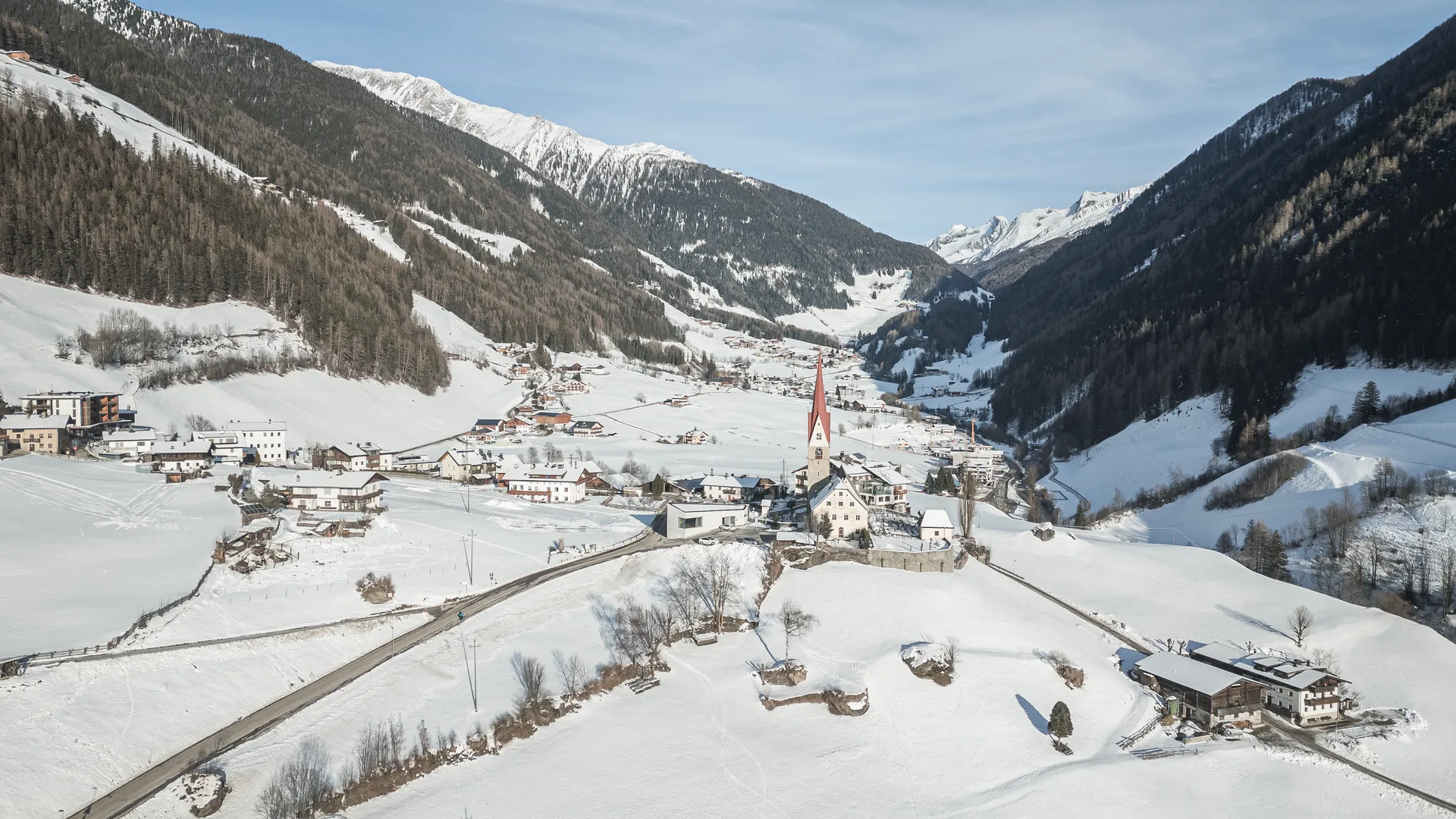 Verschneites Dorf im Ahrntal mit markanter Kirche, umgeben von Südtiroler Bergen im Winter