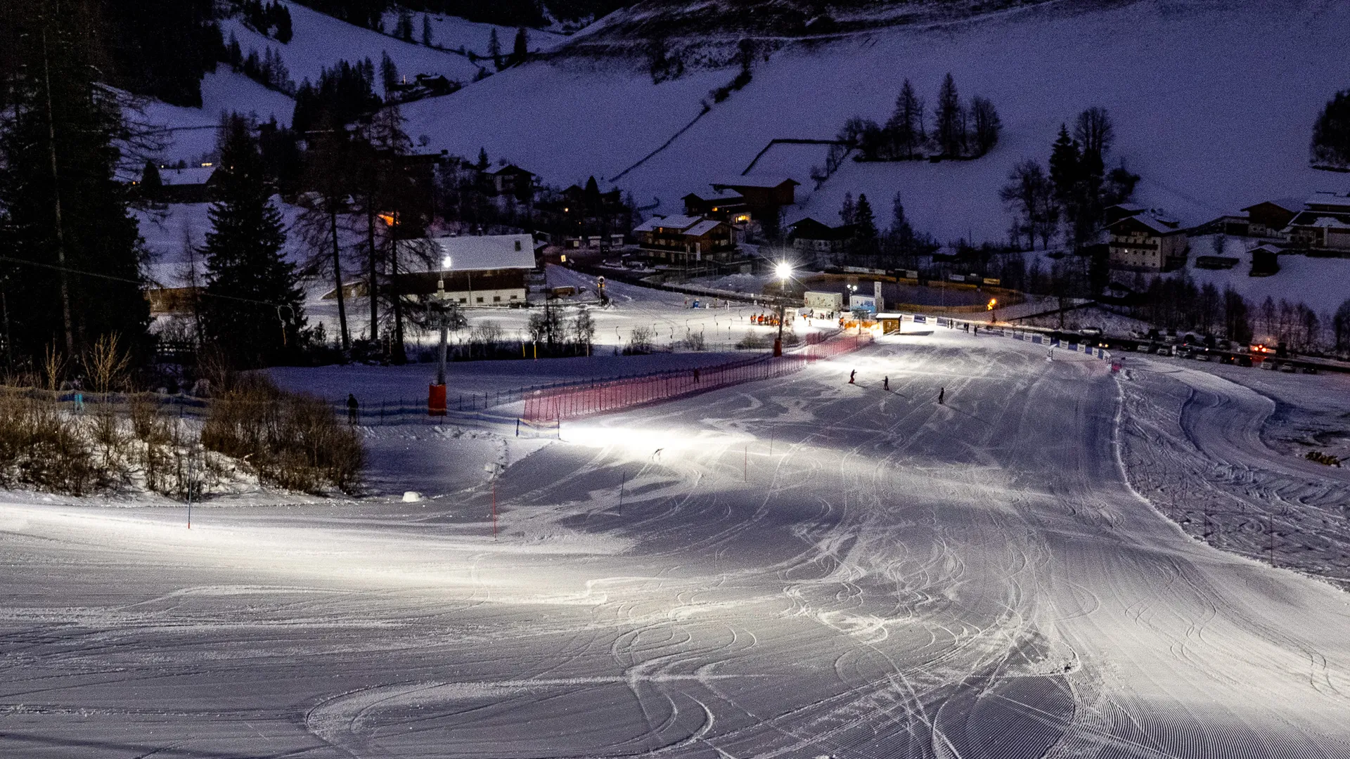Night skiing on floodlit slope at Klausberg with snow-covered village in the valley below