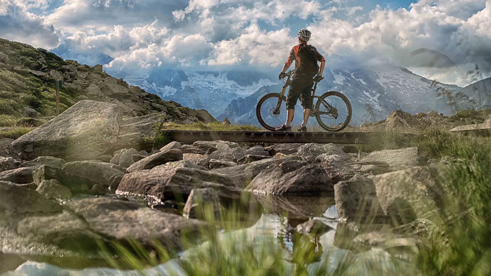 Mountain biker on wooden bridge at Klausberg with panoramic view of the Zillertal Alps in summer