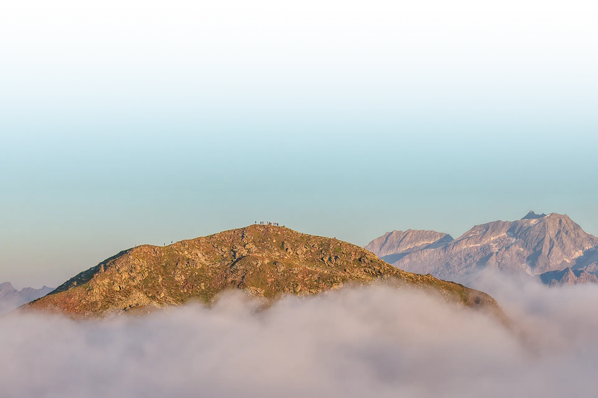 Escursionista su una vetta sopra il mare di nebbia con le Alpi della Zillertal alla luce del mattino