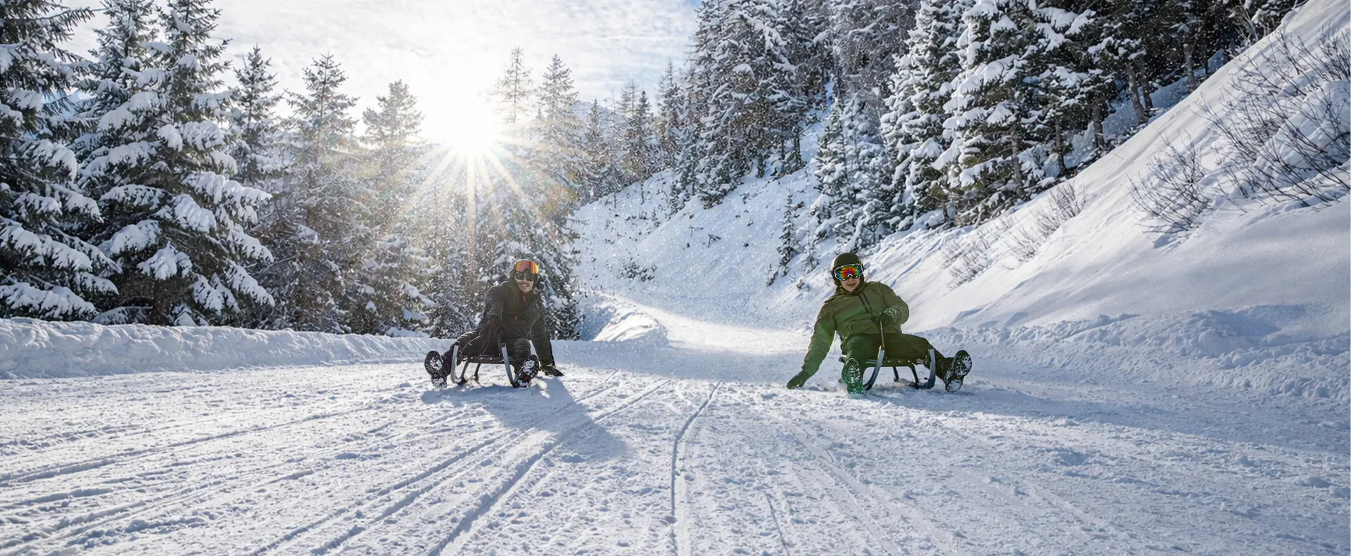 Two sledders racing through the snowy winter forest on the toboggan run in Ahrntal