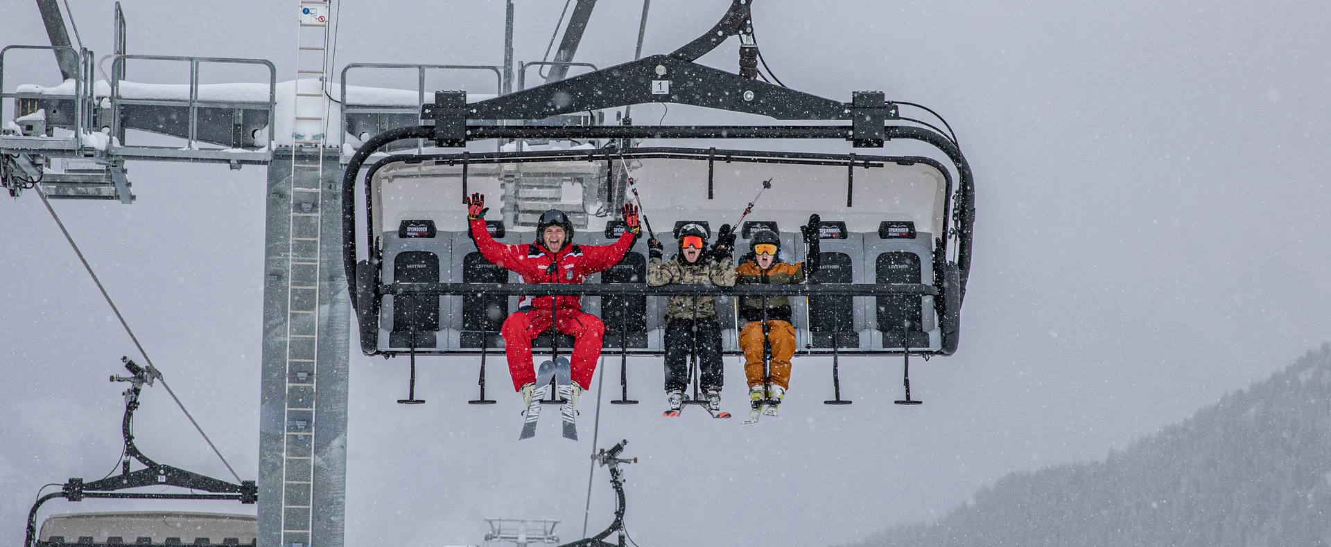 Skifahrer auf Sessellift am Speikboden bei Schneefall mit jubelndem Skilehrer in roter Uniform