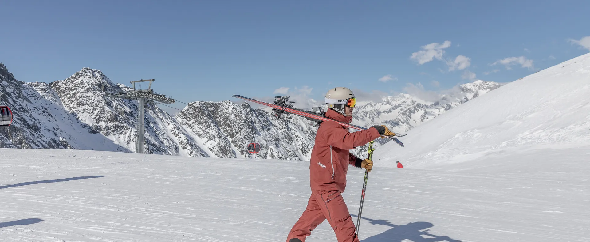 Skier with skis over the shoulder on a sunny slope at Speikboden with views of the Zillertal Alps