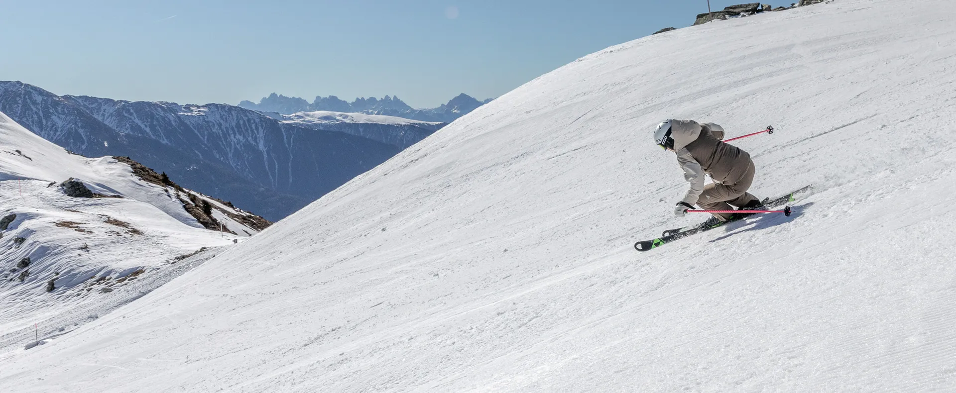 Skier in dynamic carving position on wide slope with Dolomites panorama