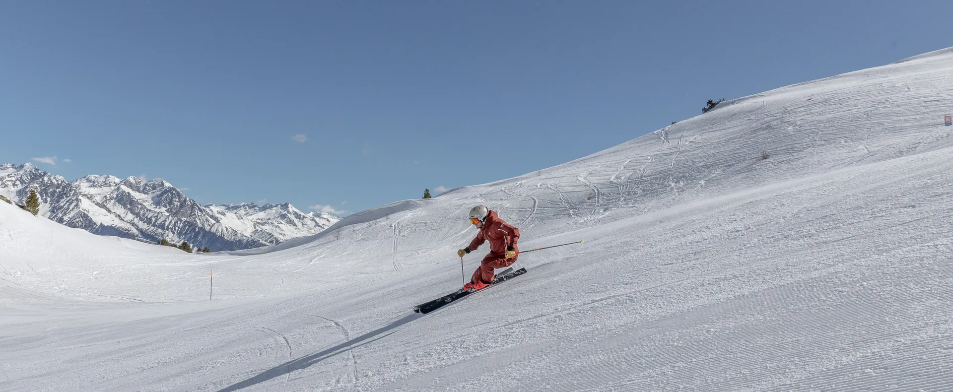 Female skier in red clothing on a freshly groomed slope at Klausberg with mountain panorama