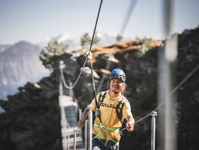 Giovane scalatore su ponte sospeso della via ferrata al Klausberg con vista sulle Alpi
