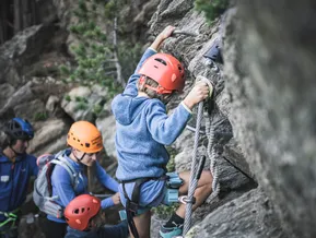 Child climbing via ferrata at Speikboden with mountain guide and family