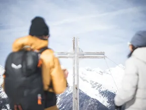 Croce di legno sulla vetta dello Speikboden con escursionisti e ampio panorama alpino in Valle Aurina