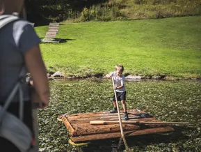 Junge stakt mit Holzfloß über Bergsee im Familienpark Klausberg