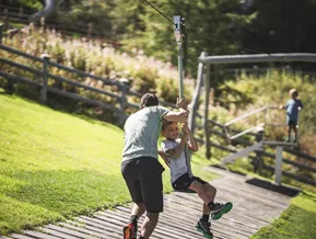 Kind auf Seilrutsche am Bergspielplatz Klausberg, Vater hilft beim Anstoßen