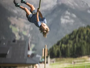 Lachendes Kind hängt kopfüber an Seilrutsche im Bergspielpark Klausberg