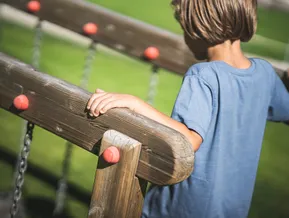 Kind spielt am Holzgeländer des Erlebnisspielplatzes im Ahrntal