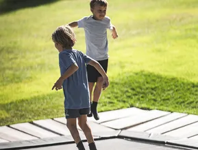 Zwei Kinder springen fröhlich auf Bodentrampolin auf grüner Wiese am Familienpark im Ahrntal