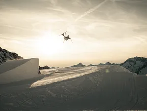 Freestyle-Skifahrer beim Backflip im Sonnenuntergang mit roten Klausberg-Gondeln im Hintergrund