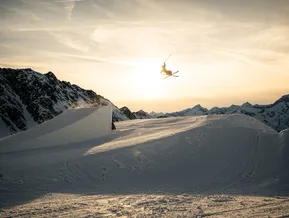 Silhouette eines Freestyle-Skifahrers beim Grab-Trick vor alpinem Panorama im Abendlicht