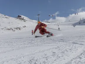 Skier in red suit carving on groomed slope with cable car in the background