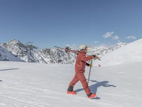 Skier with skis over the shoulder on a sunny slope at Speikboden with views of the Zillertal Alps