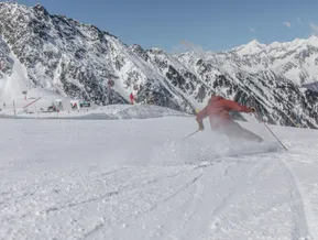 Skier in red clothing carving on a groomed slope at Klausberg with the Ahrntal mountain panorama