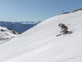 Skier in dynamic carving position on wide slope with Dolomites panorama