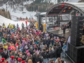 Après-Ski-Konzert mit Solist und Gitarre an der Piste, Zuschauer mit Getränken vor der Liftanlage