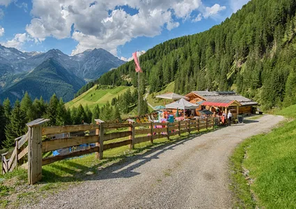 Berghütte mit Liegestühlen und Gästen in Tracht auf Almweg im Ahrntal