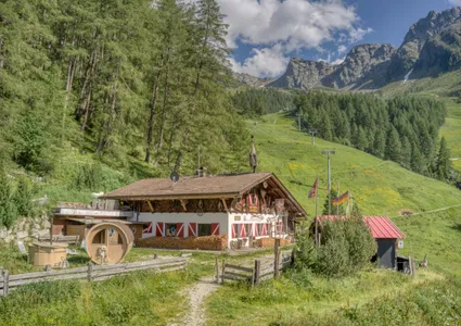 Almhütte mit Flaggen, Holzfasssauna und Lärchen am Klausberg im Sommer
