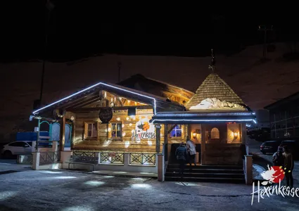 Hexenkessel Après-Ski-Bar bei Nacht beleuchtet, Schnee und Gondelbahn im Hintergrund