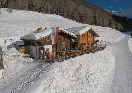 Moaregg Alm aus der Luft – Hütte an der Piste mit Gästen auf der Sonnenterrasse, Südtiroler Fahne