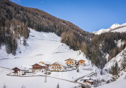 Eingeschneiter Weiler im winterlichen Ahrntal mit traditionellen Höfen und bewaldeten Berghängen