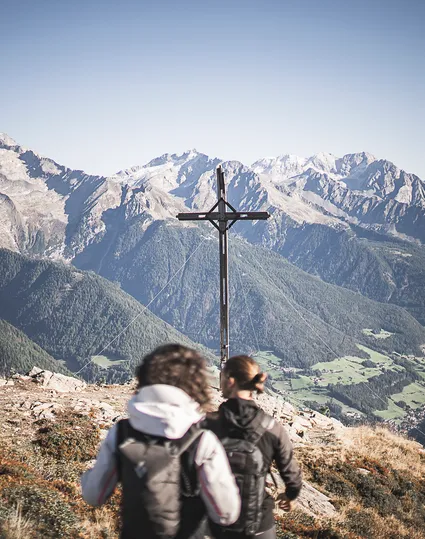 Two hikers at Speikboden summit cross with view of Zillertal Alps in summer