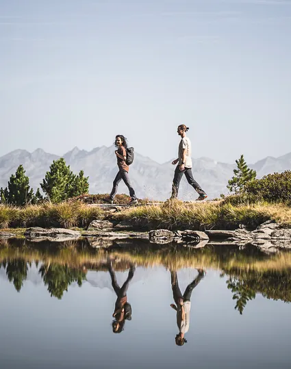 Wanderpaar am stillen Bergsee im Ahrntal mit perfekter Spiegelung der Bergkette