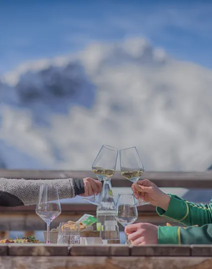 Couple toasting with white wine on a mountain hut terrace, snowy peaks in the background