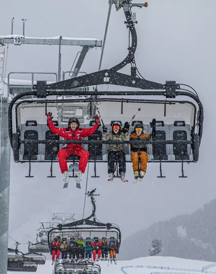 Skiers on chairlift at Speikboden during snowfall with cheering ski instructor in red uniform