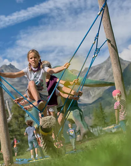 Children on rope swing at Klausberg adventure park with dinosaur figure and mountain panorama