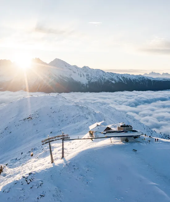 Luftaufnahme der Bergstation Sonnklar bei goldenem Sonnenaufgang über dem Wolkenmeer