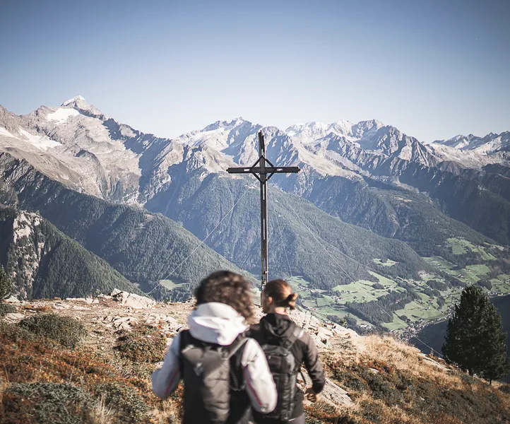 Zwei Wanderer am Gipfelkreuz des Speikbodens mit Blick auf Zillertaler Alpen im Sommer