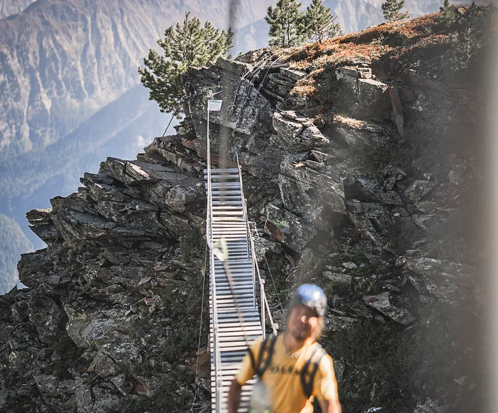 Via ferrata hiker on narrow wooden plank bridge over rock ridge, South Tyrol mountain panorama
