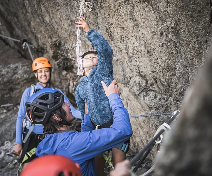Family on Ahrntal via ferrata: child rings summit bell, parents with helmets celebrate together