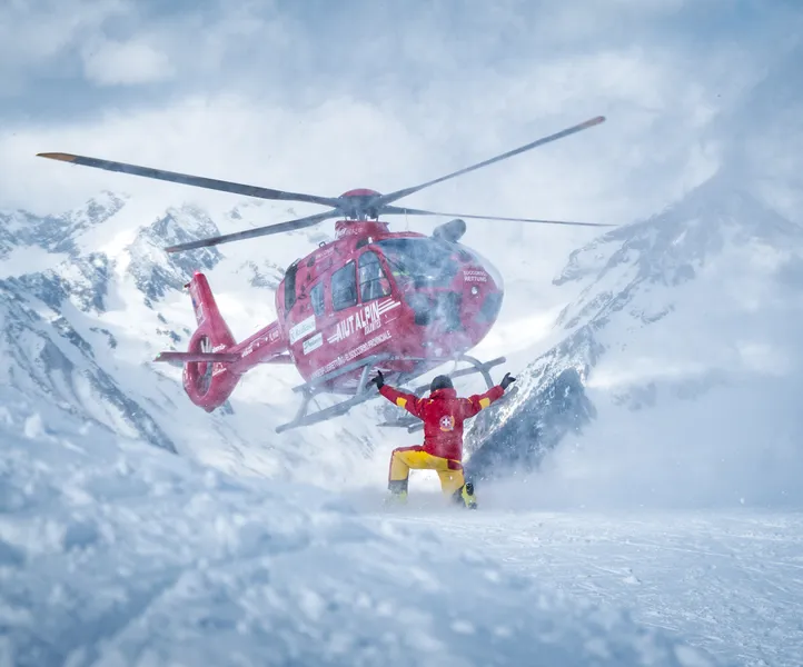 Red rescue helicopter Aiut Alpin Dolomites landing in deep snow during slope rescue operation